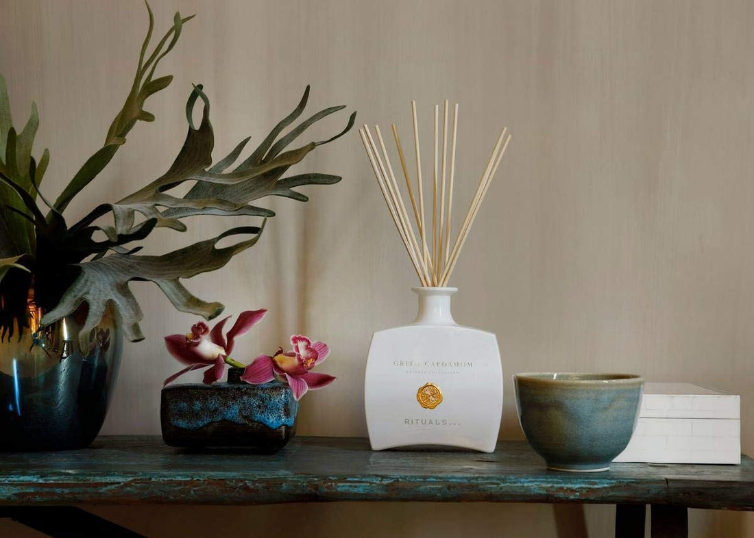Rituals reed diffuser, purple orchids, and staghorn fern on a rustic blue shelf.