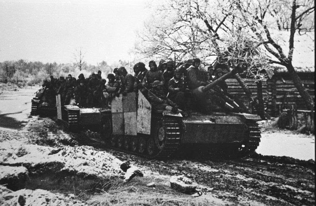 WWII historical photo of German infantry riding on a StuG III assault gun moving through a snowy, muddy landscape.
