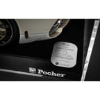 Close-up of a black Pocher branded panel or cover with a silver oval product card placed on top, alongside part of a cream-colored vehicle wheel and body panel.