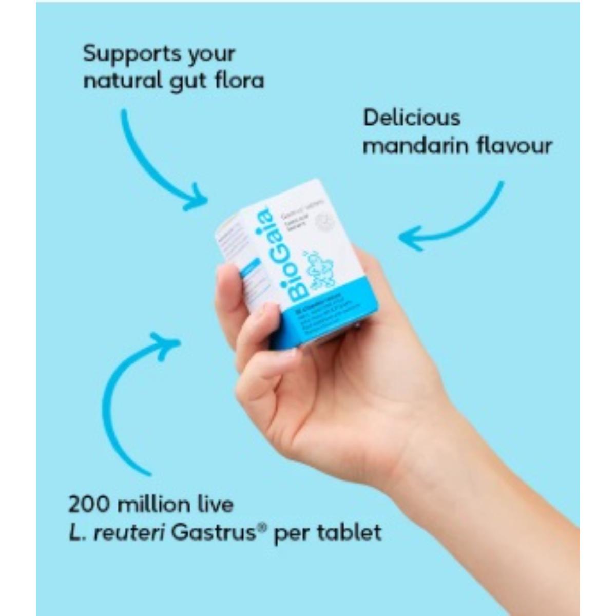 A hand holding a small white and blue Biogaea supplement box against a light blue background, with text callouts describing gut health benefits and mandarin flavor.