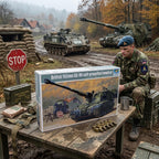 A model kit box for a British 155mm AS-90 self-propelled howitzer is displayed on a wooden table outdoors, surrounded by military-themed props including a stop sign, sandbags, and model accessories. A soldier in camouflage and a blue beret sits next to the table, with real military tanks visible in the muddy background.