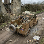 A detailed model of a vintage military truck in a muddy outdoor diorama setting, positioned next to a stone ruin and cobblestone road with miniature debris.