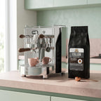 Facino Espresso machine with two pink cups and a bag of Italian gourmet coffee on a kitchen counter.
