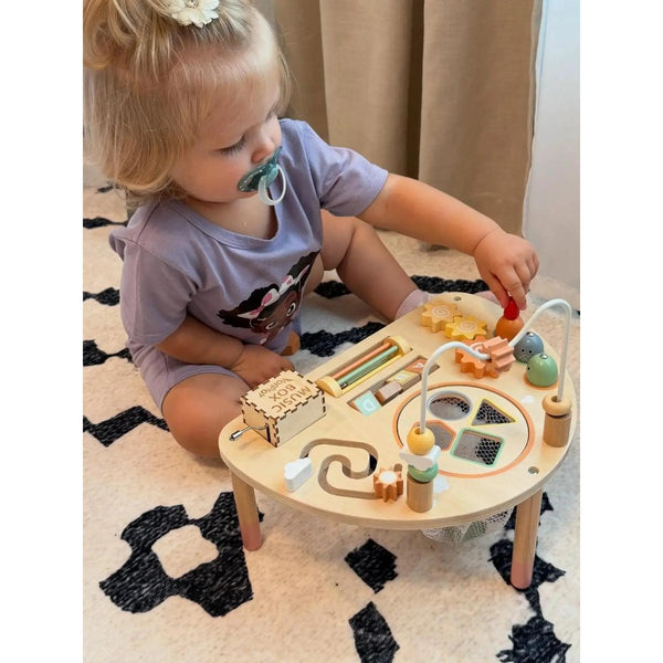 Child playing with a wooden activity table on a patterned rug.