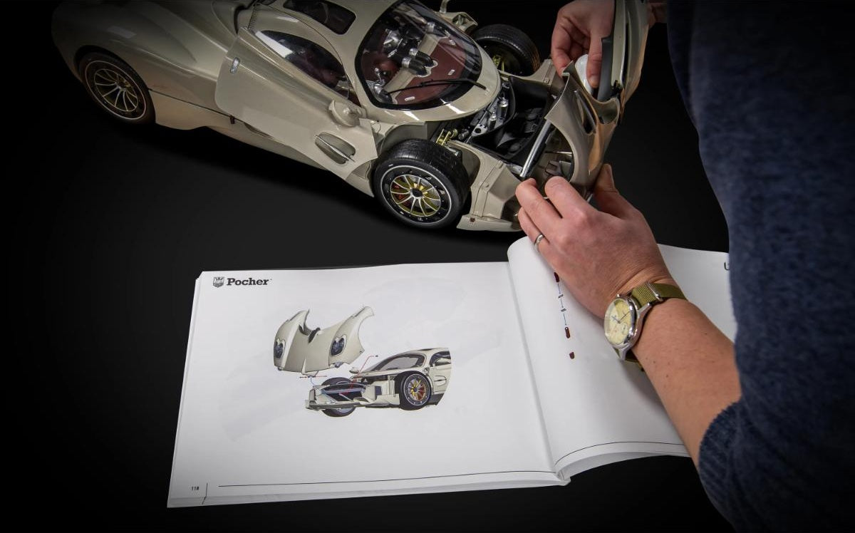 A person's hands are shown assembling a detailed model of a  pocher-BUNDLEP16-pagani-utopia-coupecar, with an open reference book displaying the original sketch and design of the vehicle on a black background.
