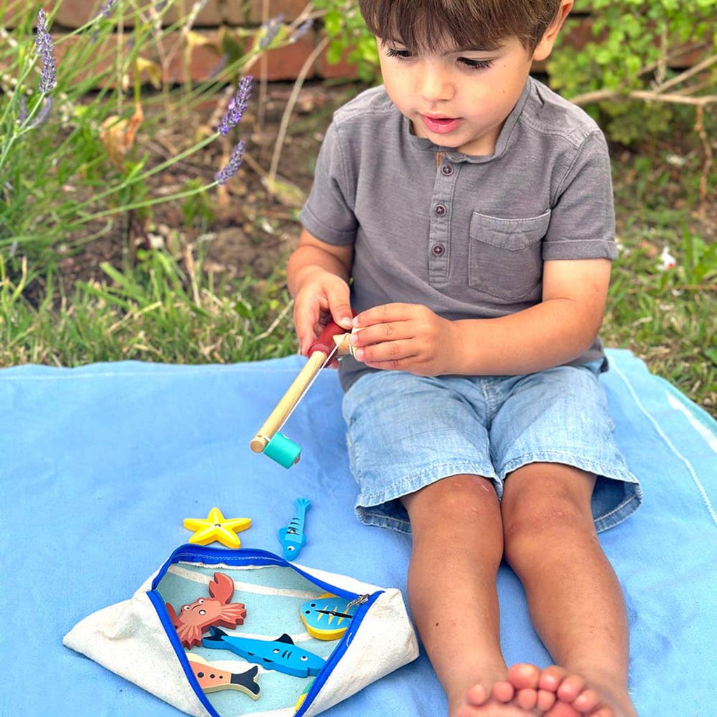 Child playing with a fishing toy set outdoors on a blue blanket.